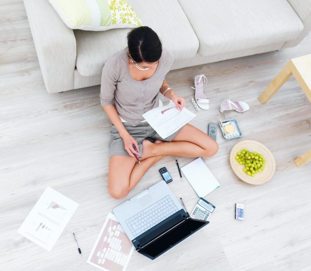 Business woman sitting in house with laptop,beside sofa High angle view of businesswoman sitting in house with laptop and documents