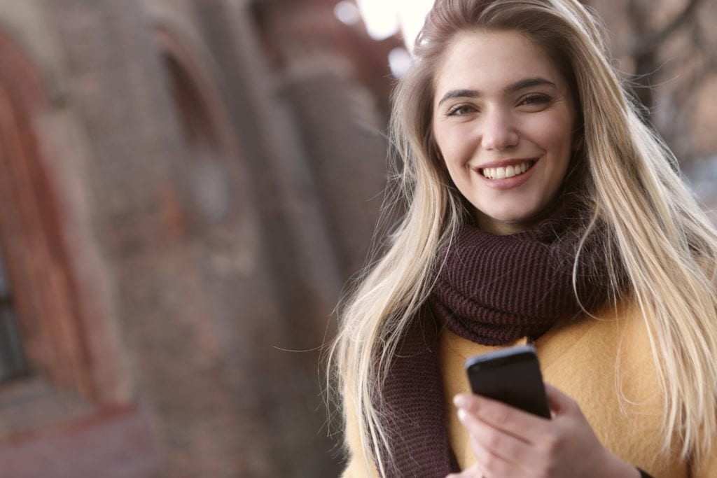 Woman smiling with a neck scarf and cell phone
