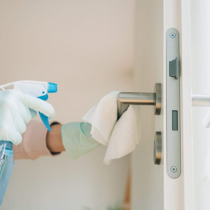 Woman cleaning a door handle with a disinfection spray